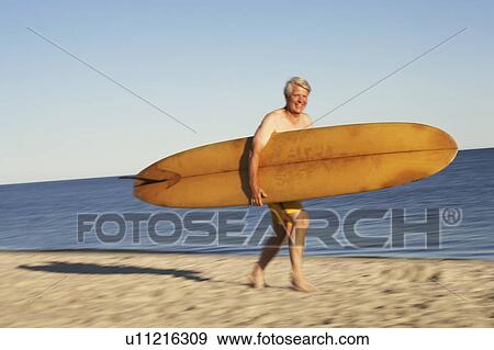 Portrait of a mature man holding a surfboard and walking on the beach View Large Photo Image Stock Photo - Portrait of a mature man holding a surfboard and walking on the beach. Fotosearch
