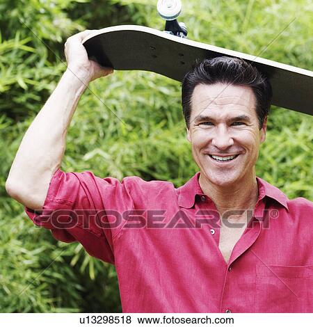 Portrait of a mature man holding a skateboard on his head and smiling View Large Photo Image Stock Photo - Portrait of a mature man holding a skateboard on his head and smiling. Fotosearch