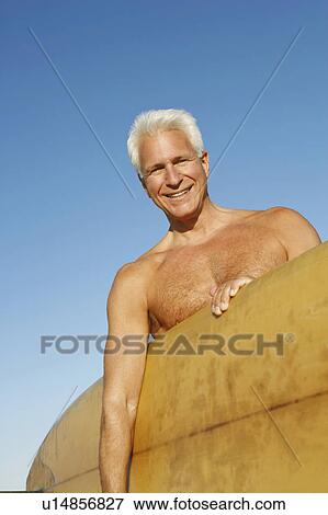 Portrait of a mature man holding a surfboard under his arm View Large Photo Image Stock Photo - Portrait of a mature man holding a surfboard under his arm. Fotosearch