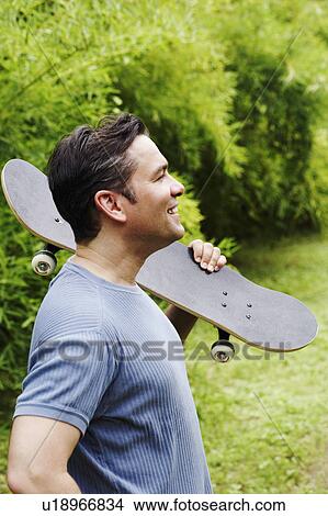 Side profile of a mature man carrying a skateboard on his shoulder and smiling View Large Photo Image Picture - Side profile of a mature man carrying a skateboard on his shoulder and smiling. Fotosearch