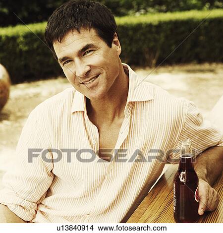 Close-up of a mature man sitting at a table and holding bottle of wine View Large Photo Image Picture - Close-up of a mature man sitting at a table and holding bottle of wine. Fotosearch