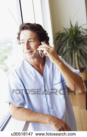 Stock Photo - Close-up of a mature man standing beside a window and talking on a mobile phone. Fotosearch