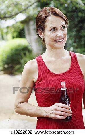 Close-up of a mature woman holding a bottle of wine and smiling View Large Photo Image Stock Image - Close-up of a mature woman holding a bottle of wine and smiling. Fotosearch
