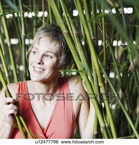 Stock Photo - Close-up of a mature woman holding bamboo plants and smiling. Fotosearch