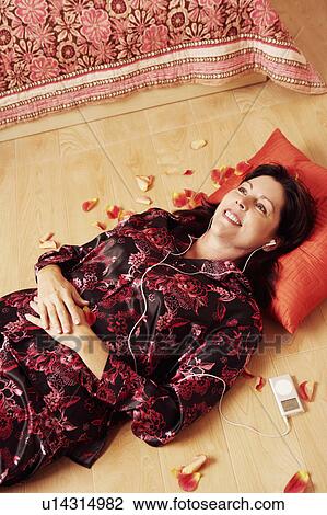 Stock Image - High angle view of a mature woman lying on a wooden floor and listening to an MP3 player. Fotosearch