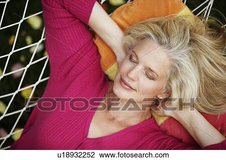 Stock Image - High angle view of a mature woman sleeping in a hammock. Fotosearch