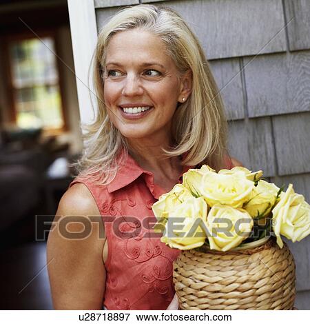 Mature woman holding flowers in a vase and smiling View Large Photo Image Stock Photo - Mature woman holding flowers in a vase and smiling. Fotosearch