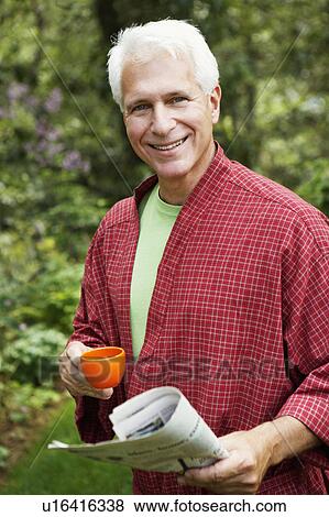 Stock Photo - Portrait of a mature man holding a newspaper and a cup of tea. Fotosearch