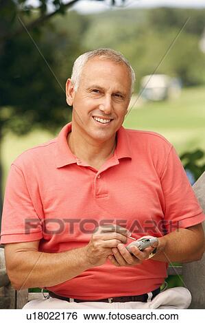 Stock Photograph - Portrait of a mature man using a personal data assistant in a park. Fotosearch