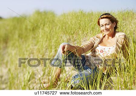 Stock Photo - Portrait of a mature woman sitting on the beach. Fotosearch