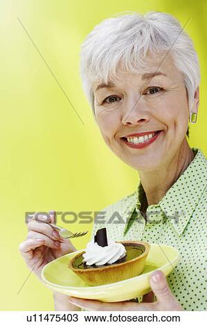 Stock Image - Portrait of a senior woman eating a tart with a fork. Fotosearch