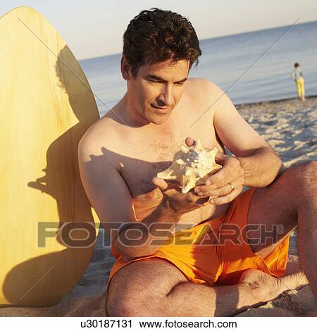 Stock Image - Close-up of a mature man looking at a seashell. Fotosearch