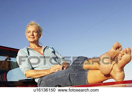 Low angle view of a mature woman sitting on the bonnet of a sports utility vehicle and looking away View Large Photo Image Stock Image - Low angle view of a mature woman sitting on the bonnet of a sports utility vehicle and looking away. Fotosearch