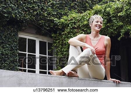 Stock Image - Mature woman sitting on a wall and smiling. Fotosearch