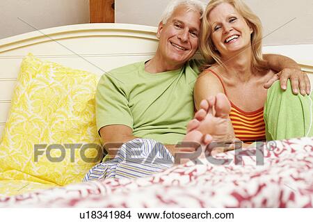 Picture - Portrait of a mature couple sitting on the bed and smiling. Fotosearch