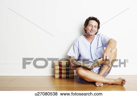 Stock Photo - Portrait of a mature man sitting on the floor with a book and smiling. Fotosearch
