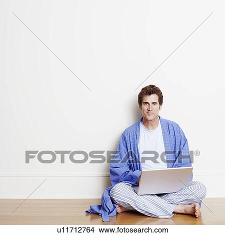Portrait of a mature man sitting cross-legged on the floor and using a laptop View Large Photo Image Picture - Portrait of a mature man sitting cross-legged on the floor and using a laptop. Fotosearch