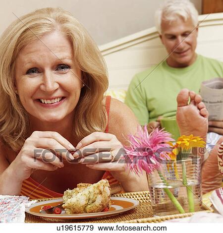 Portrait of a mature woman having breakfast in bed with a mature man sitting behind her View Large Photo Image Stock Photo - Portrait of a mature woman having breakfast in bed with a mature man sitting behind her. Fotosearch