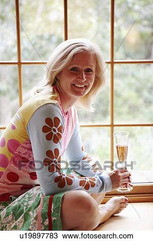 Portrait of a mature woman holding a champagne flute and smiling View Large Photo Image Stock Image - Portrait of a mature woman holding a champagne flute and smiling. Fotosearch