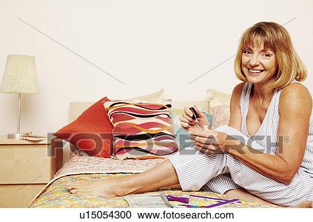 Stock Image - Portrait of a mature woman holding nail polish and smiling. Fotosearch