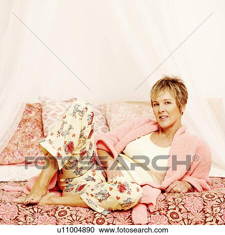 Stock Image - Portrait of a mature woman leaning on the bed. Fotosearch