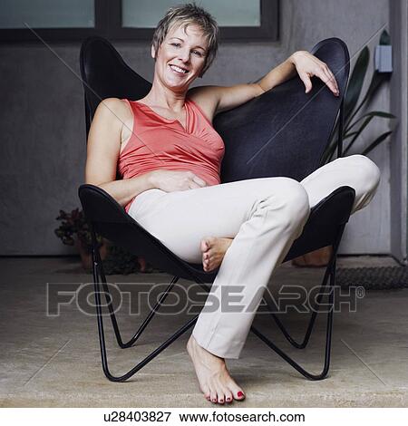 Stock Photo - Portrait of a mature woman sitting on a chair and smiling. Fotosearch