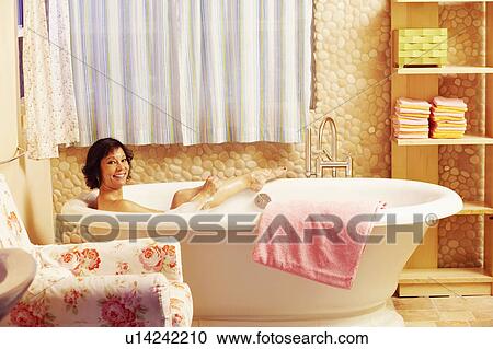 Stock Image - Portrait of a mature woman using a sponge in a bathtub and smiling. Fotosearch
