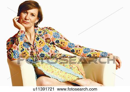 Stock Image - Portrait of a mid adult woman sitting in an armchair with her hand on her chin. Fotosearch