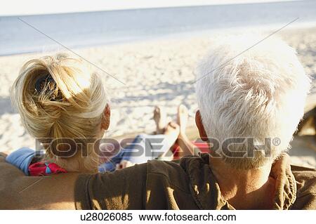 Rear view of a mature couple sitting on the beach View Large Photo Image Stock Photography - Rear view of a mature couple sitting on the beach. Fotosearch