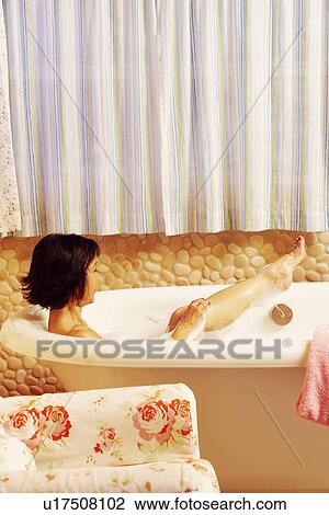 Stock Image - Side profile of a mature woman using a sponge in a bathtub. Fotosearch