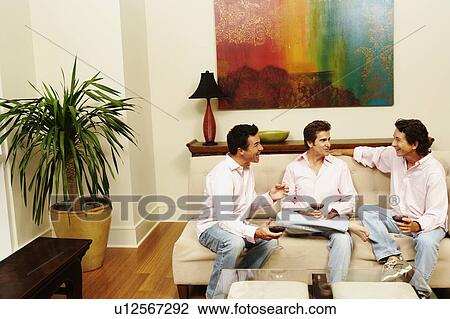 Stock Image - Three mature men sitting together and holding glasses of wine. Fotosearch