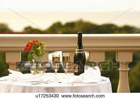 Stock Image - Champagne bottle and two champagne flutes with a vase on the table. Fotosearch