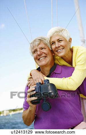 Stock Photo - Mature woman embracing a mature man from behind in a boat and smiling. Fotosearch