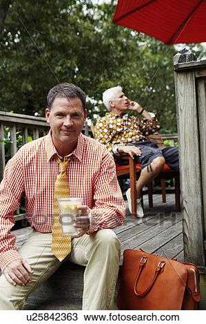 Stock Image - Portrait of a businessman holding a mug of milkshake and smiling. Fotosearch