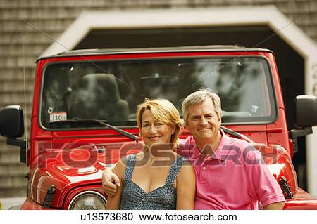 Stock Image - Portrait of a mature couple in front of a sports utility vehicle and smiling. Fotosearch