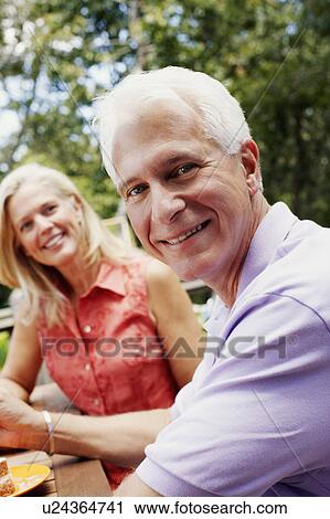 Stock Image - Portrait of a mature couple sitting at the table and smiling. Fotosearch