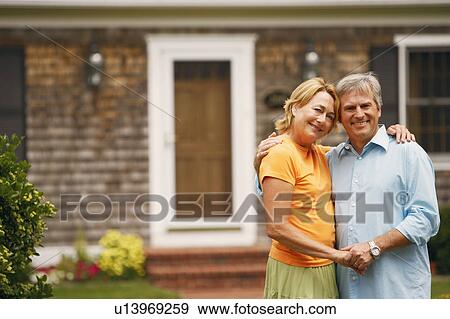 Stock Photo - Portrait of a mature couple standing with their arms around each other in front of a house. Fotosearch