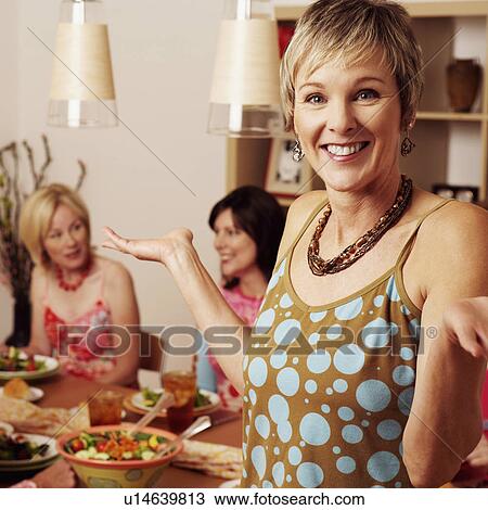 Portrait of a mature woman gesturing and her friends sitting at the dining table in the background View Large Photo Image Stock Image - Portrait of a mature woman gesturing and her friends sitting at the dining table in the background. Fotosearch