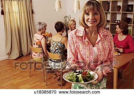 Portrait of a mature woman holding a plate of salad and her friends sitting behind her View Large Photo Image Stock Image - Portrait of a mature woman holding a plate of salad and her friends sitting behind her. Fotosearch