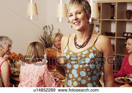 Portrait of a mature woman holding a glass of cocktail and her friends sitting at a dining table in the background View Large Photo Image Stock Photo - Portrait of a mature woman holding a glass of cocktail and her friends sitting at a dining table in the background. Fotosearch
