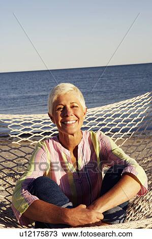 Stock Image - Portrait of a mature woman sitting in a hammock and smiling. Fotosearch