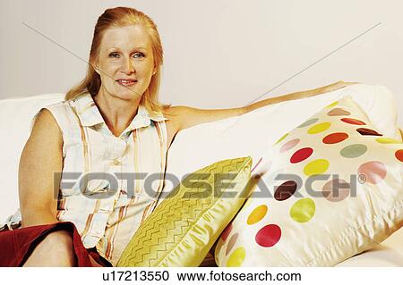 Stock Image - Portrait of a mature woman sitting on a couch and smiling. Fotosearch