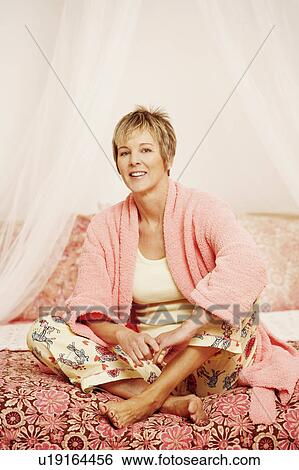 Stock Photograph - Portrait of a mature woman sitting on the bed. Fotosearch