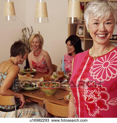 Portrait of a mature woman smiling and her friends sitting at the dining table in the background View Large Photo Image Stock Image - Portrait of a mature woman smiling and her friends sitting at the dining table in the background. Fotosearch