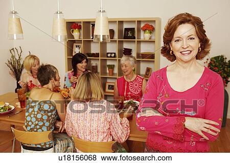 Stock Photo - Portrait of a mature woman smiling and her friends sitting at the dining table in the background. Fotosearch