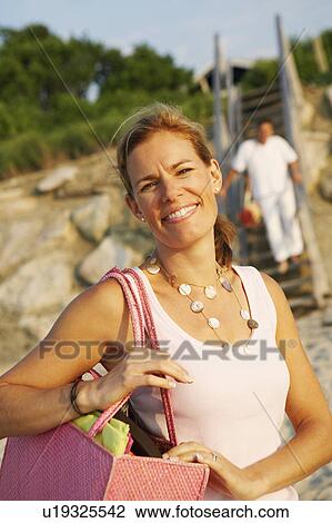 Portrait of a mid adult woman carrying a bag and smiling on the beach View Large Photo Image Stock Image - Portrait of a mid adult woman carrying a bag and smiling on the beach. Fotosearch