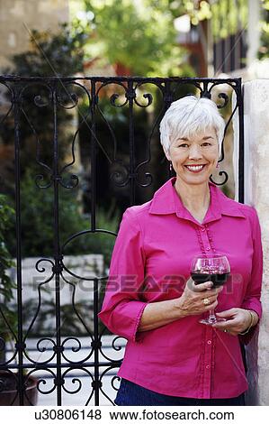 Stock Photo - Portrait of a senior woman holding a glass of red wine. Fotosearch