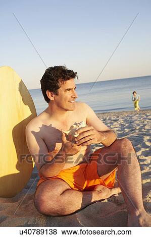 Close-up of a mature man sitting on the beach and holding a seashell View Large Photo Image Stock Photo - Close-up of a mature man sitting on the beach and holding a seashell. Fotosearch