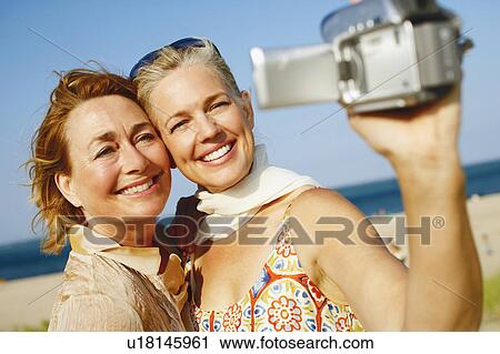 Stock Image - Close-up of two mature women taking a picture of themselves on the beach. Fotosearch