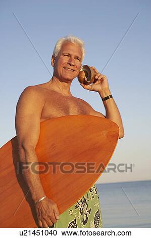 Low angle view of a mature man holding a surfboard and seashell View Large Photo Image Stock Image - Low angle view of a mature man holding a surfboard and seashell. Fotosearch